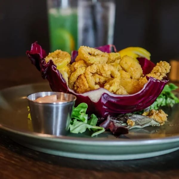 Crispy fried calamari served in a radicchio cup with a side of dipping sauce and lemon.