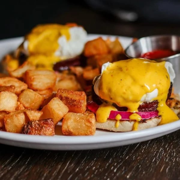 Eggs Benedict with hollandaise sauce, bacon, and pickled onions, served with crispy home fries.