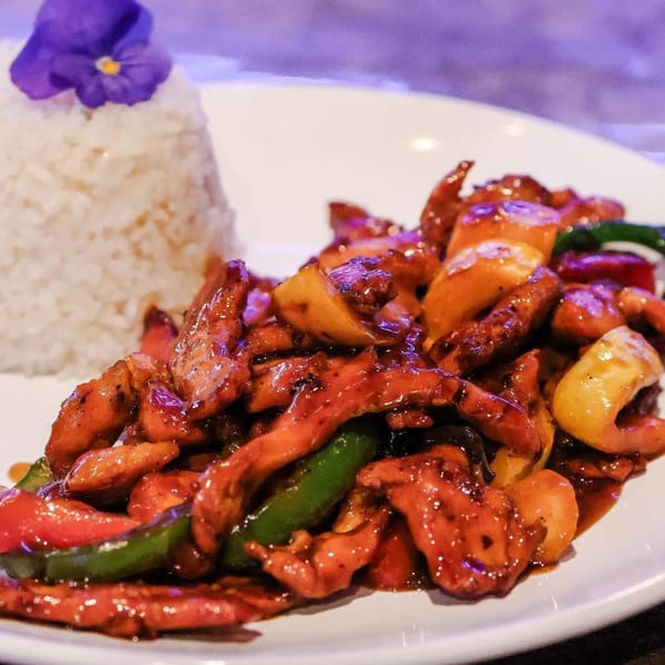 Sweet and sour chicken with bell peppers and rice, garnished with a purple flower.
