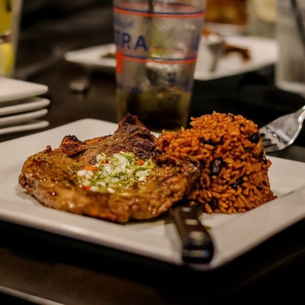 Grilled pork chop with green relish and a side of red rice with black beans.