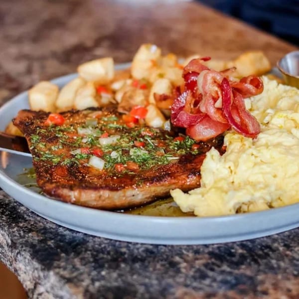 A breakfast plate with steak, scrambled eggs, crispy bacon, and home fries on a gray plate.