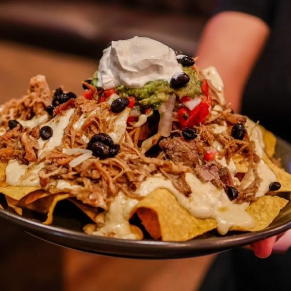 A plate of loaded nachos with pulled pork, cheese sauce, black beans, guacamole, and sour cream.