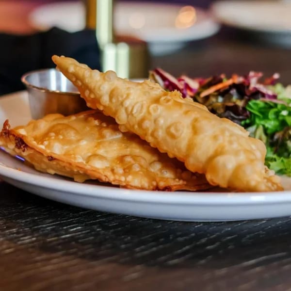 Two golden-brown fried empanadas with a side salad and dipping sauce on a white plate.