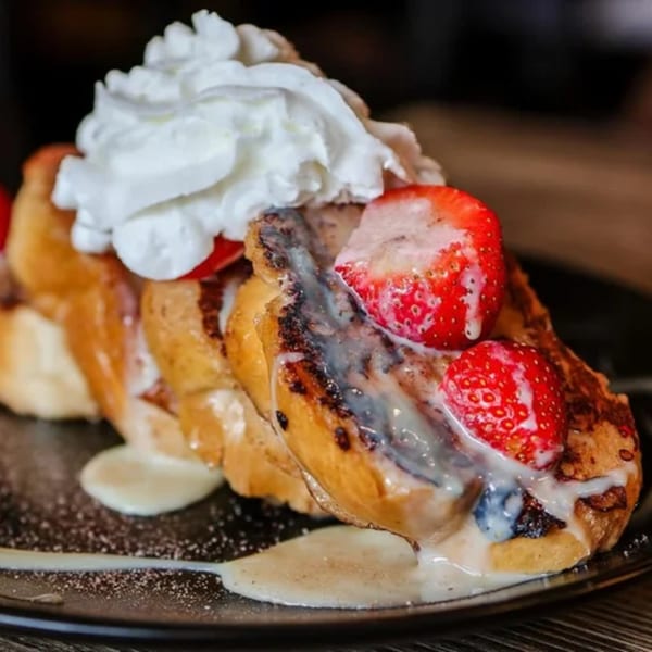 Golden French toast topped with whipped cream, fresh strawberries, and a sweet drizzle.