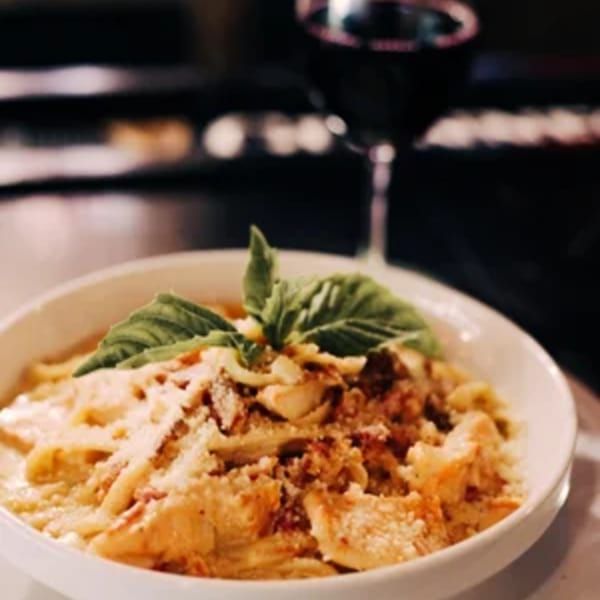 Creamy pasta dish topped with fresh basil and grated cheese, with a glass of red wine.