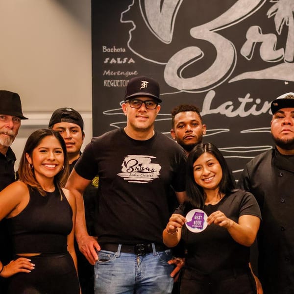 Seven restaurant staff members, including chefs and servers, pose together in front of a chalkboard menu.
