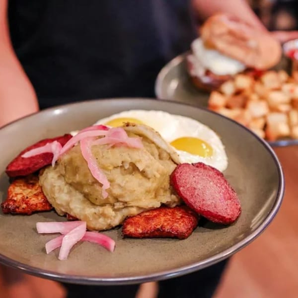 A plate of mangu with fried eggs, salami, fried cheese, and pickled red onions.