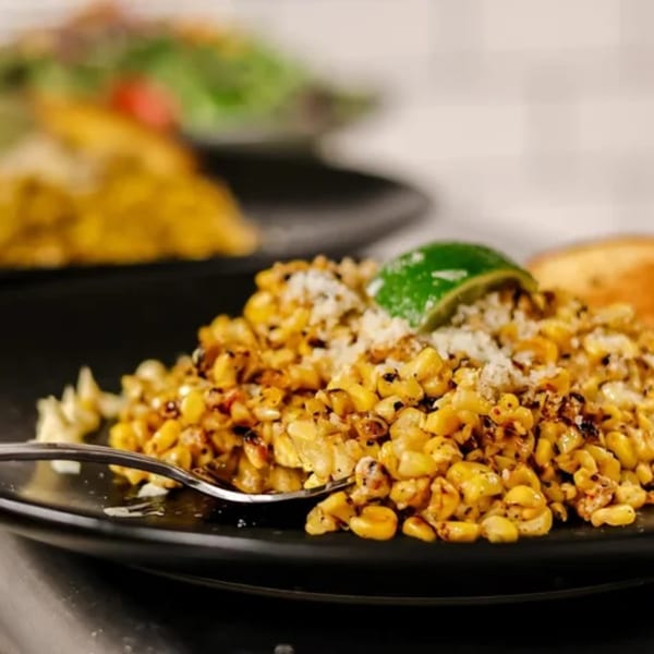 Close-up of roasted corn kernels with cheese and a lime wedge on a black plate.